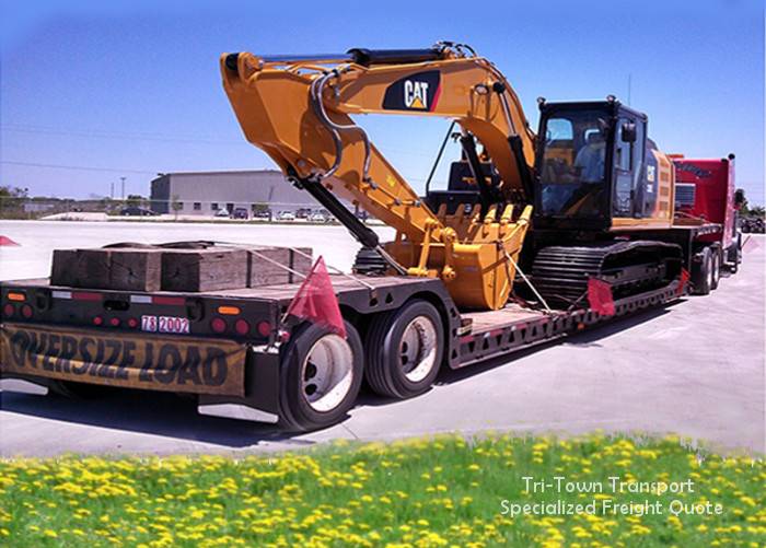 A backhoe on a flatbed trailer in front of a field of yellow flowers on a sunny day