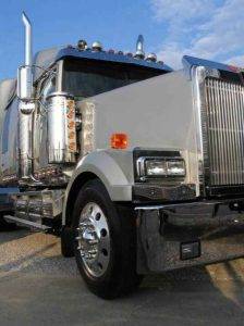A silver big rig truck shown close up parked on a paved lot.